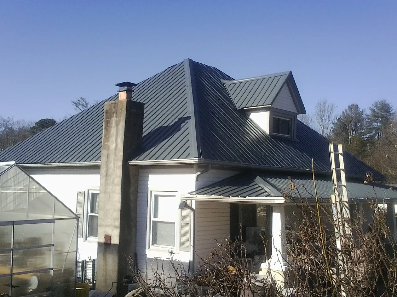 Dark blue standing seam metal roof on a white farmhouse with dormer — Slate & Tile Roof Repair by Roofing Brothers in Woolstock