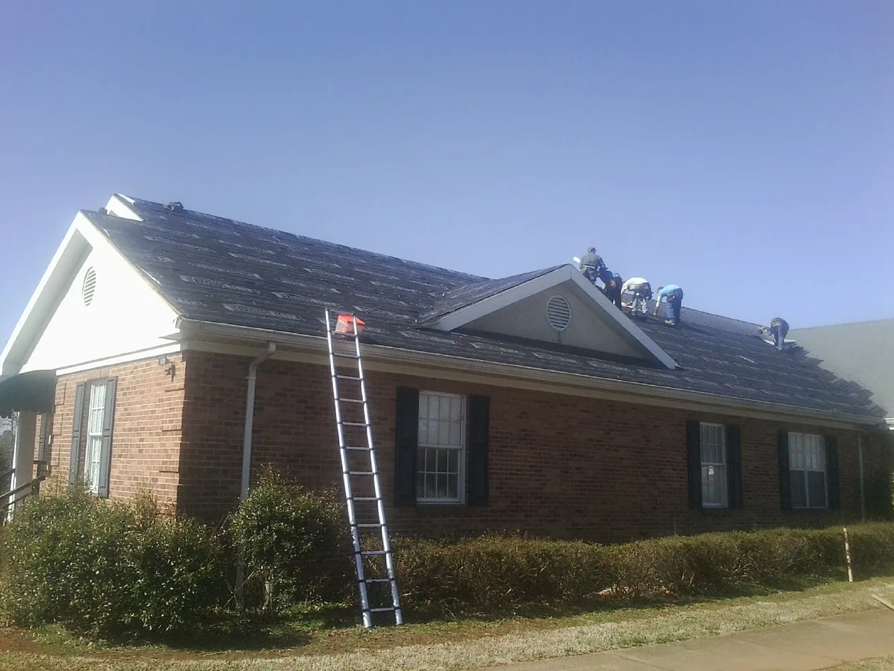 Crew tearing shingles off a brick ranch roof with a ladder set — Emergency Roof Repair work by our crew in Woolstock