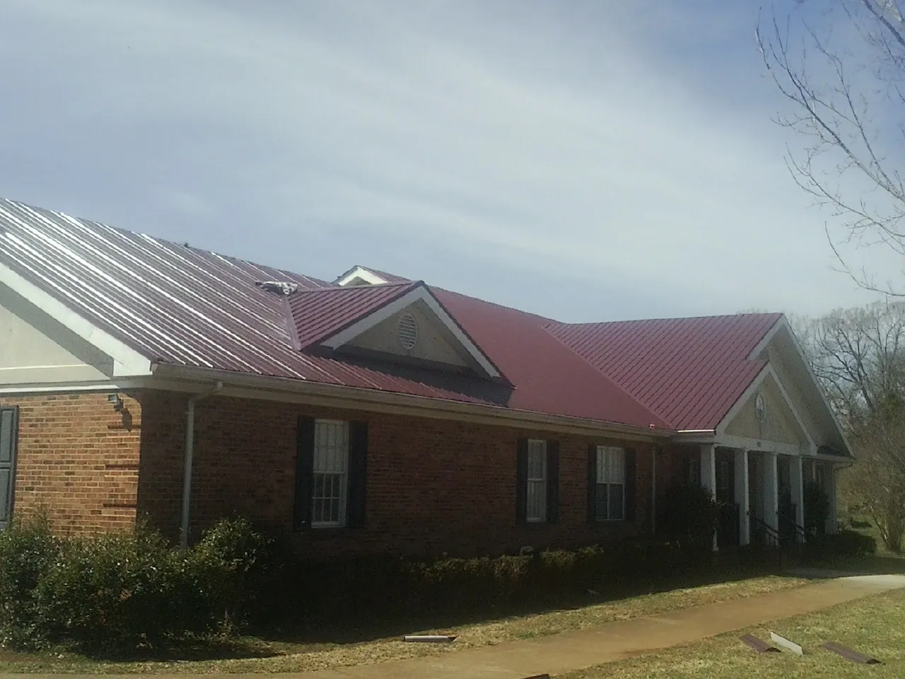 Red metal roof with gabled entries on a long brick building, from a Hail Damage Roof Repair job in Woolstock
