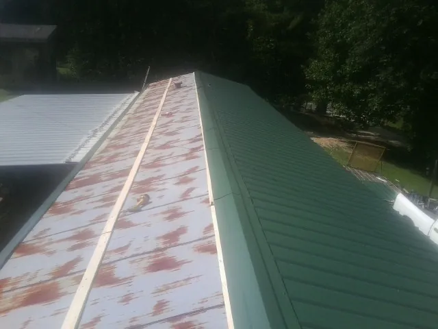 Old rusted panels beside newly installed green metal roofing — Wind Damage Roof Repair by Roofing Brothers in Woolstock