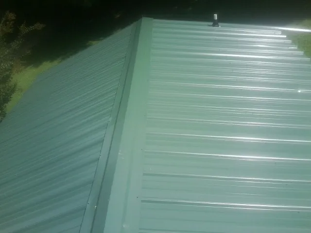 New green metal panels meeting at the ridge of a roof — Flat Roof Repair work by our crew in Woolstock