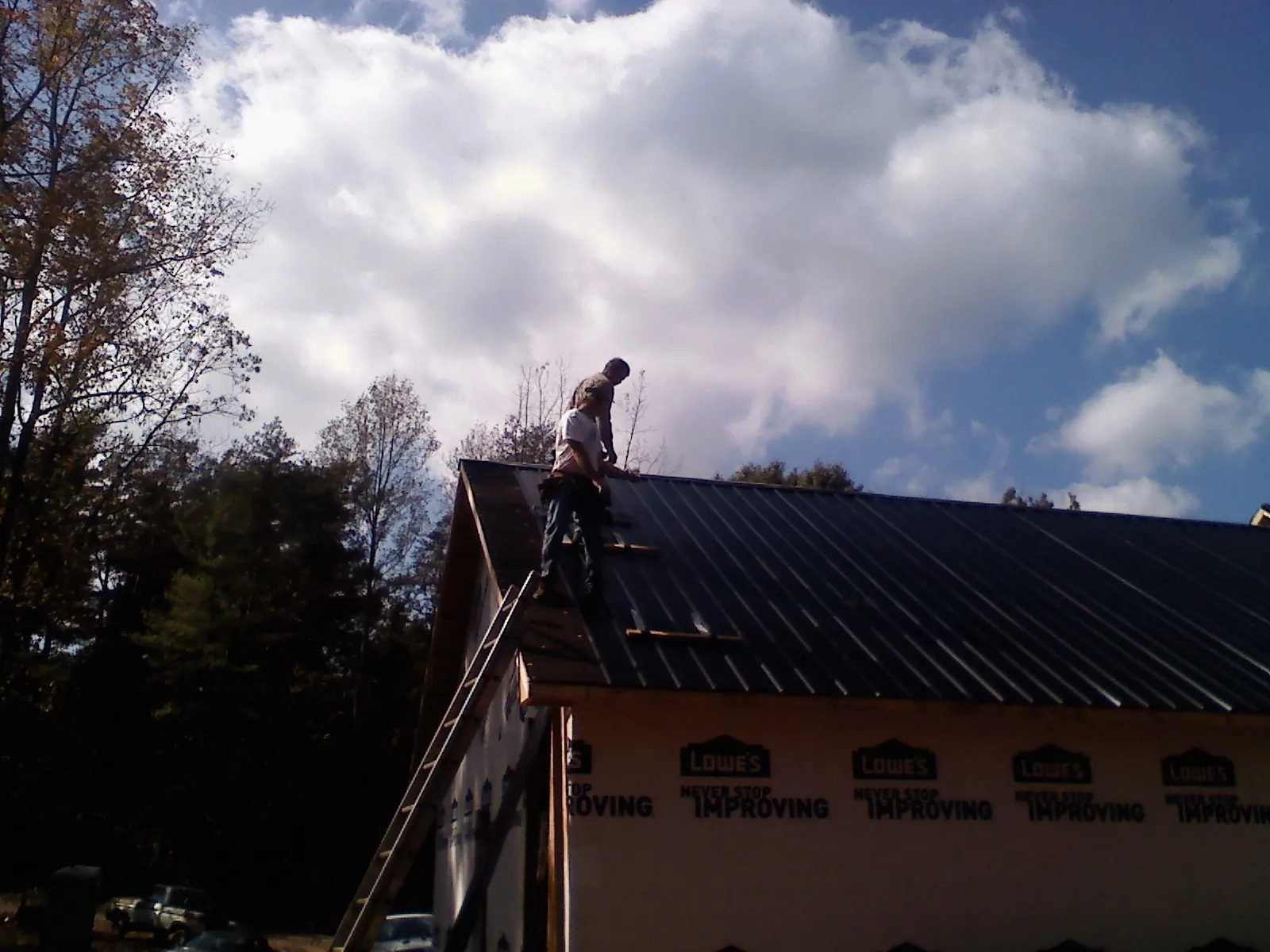 Roofer fastening dark metal panels high against a cloudy sky, from a Roof Inspection job in Woolstock