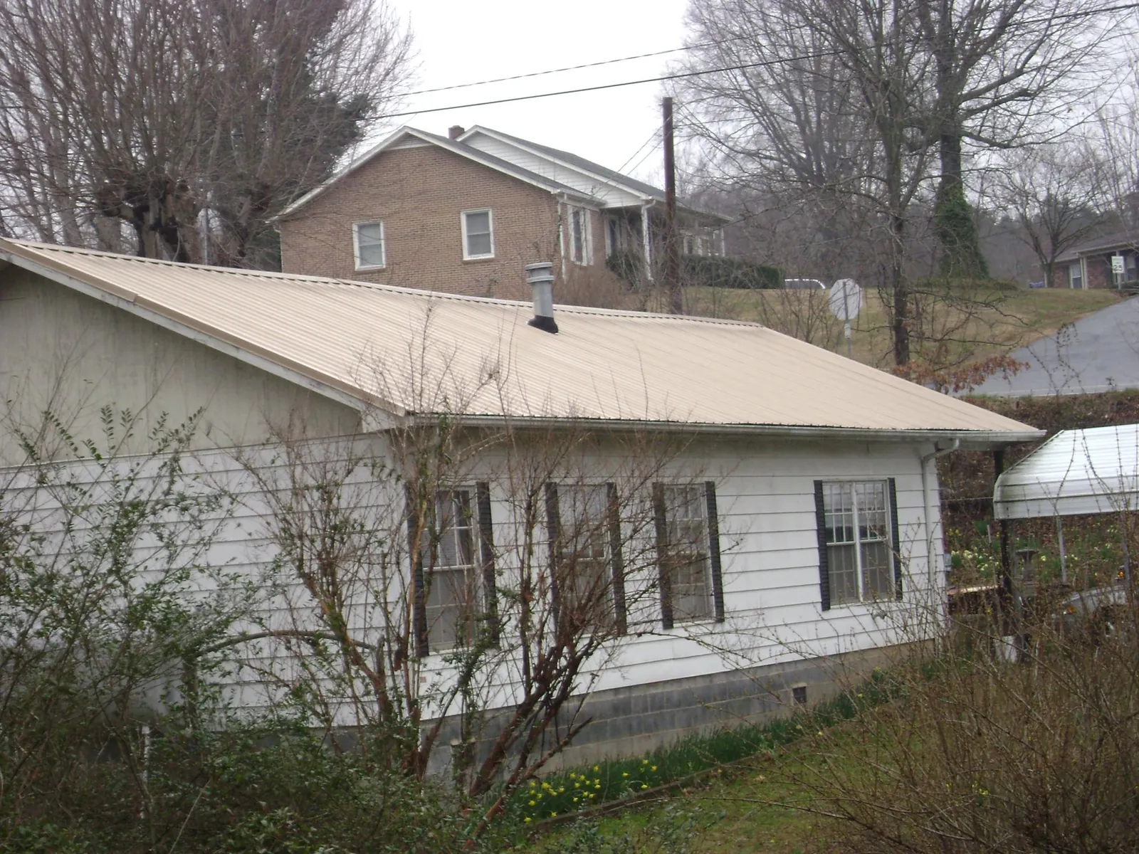Tan metal roof on a white sided house set into a hillside — Commercial Roofing by Roofing Brothers in Woolstock