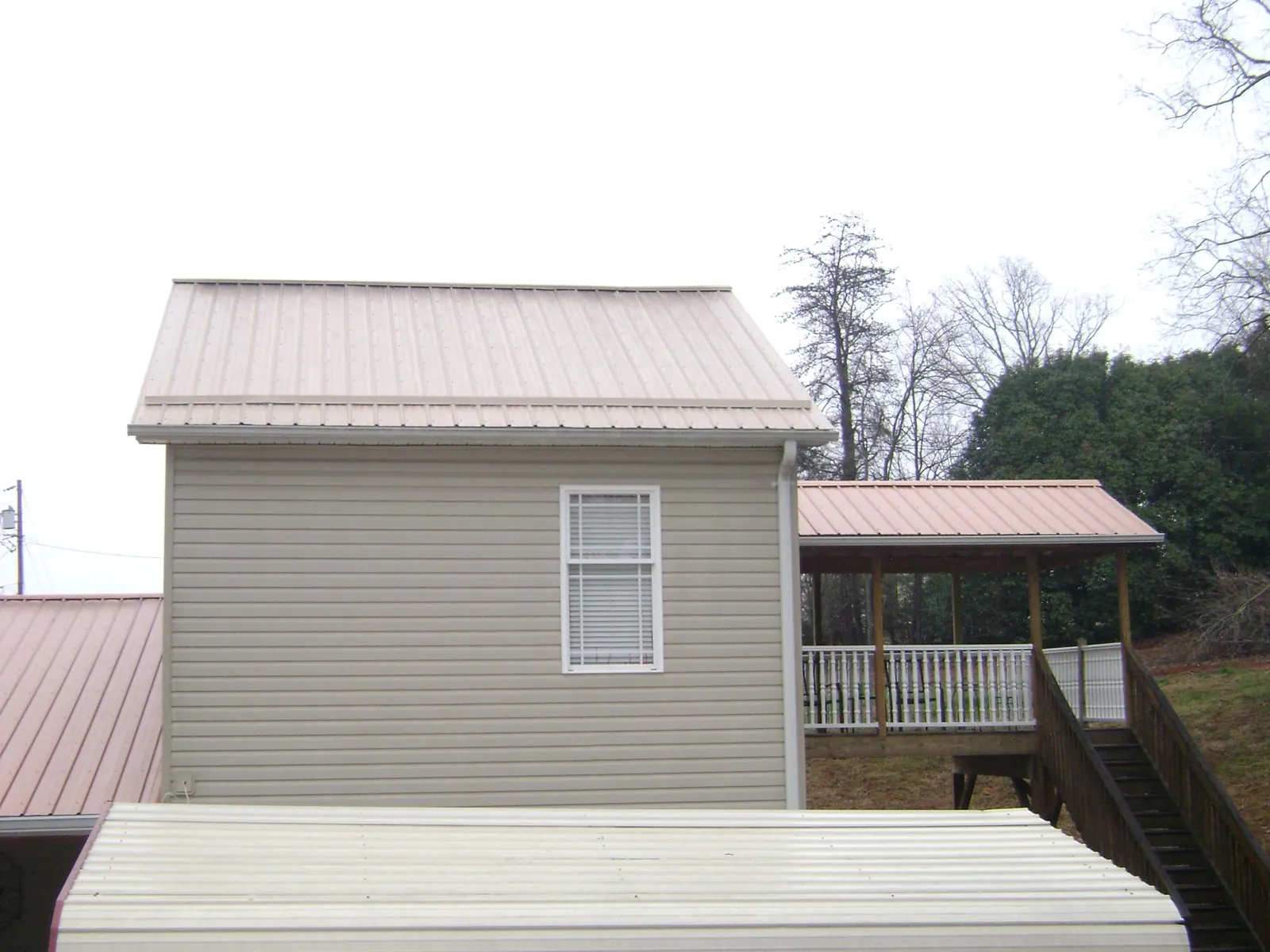 Tan metal roofs on a two story addition and attached porch, from a Roof Replacement job in Woolstock