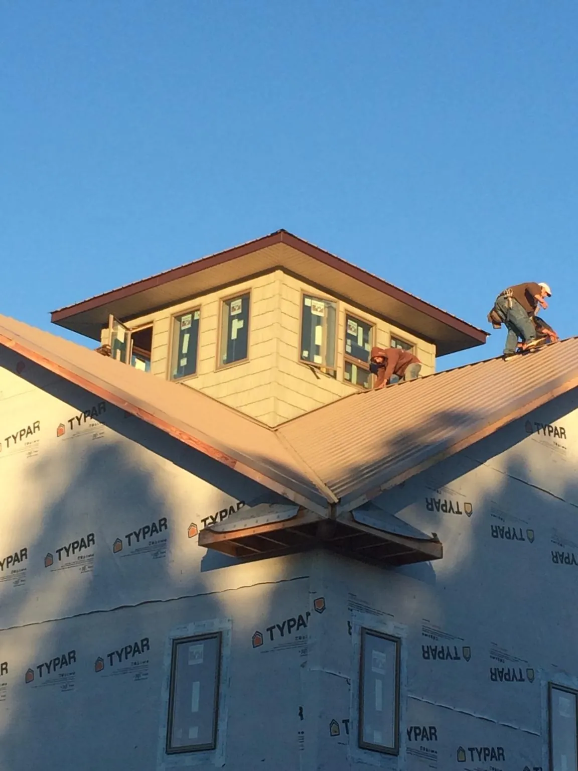 Roofers working around a rooftop cupola on a new metal roof at sunset — Roof Waterproofing in Woolstock by Roofing Brothers